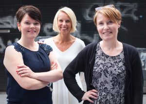 Tre medarbetare i kommunikationsteamet ler och tittar in i kameran.r in i k