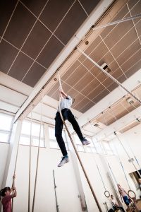 Ett barn klättrar mot taket i en lian i en gymnasitiksal.