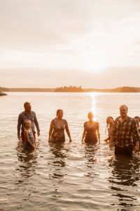 Några människor som står i havet vid solnedgången.