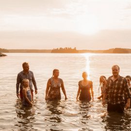 En liten grupp människor som står i vattnet under en solnedgång.