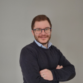 En porträttbild på Joel Johansson. Han ler och har armarna korsade över bröstet.