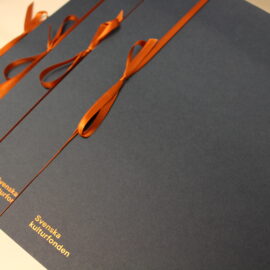 Fyra mötkblåa diplom på ett bord.Diplomen har orangea silkesband.