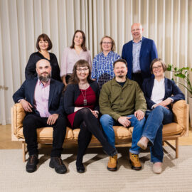 Kulturfondens åtta ombudsmän sitter i en soffa eller står bakom ryggstödet. Alla tittar in i kameran och ser glada ut.