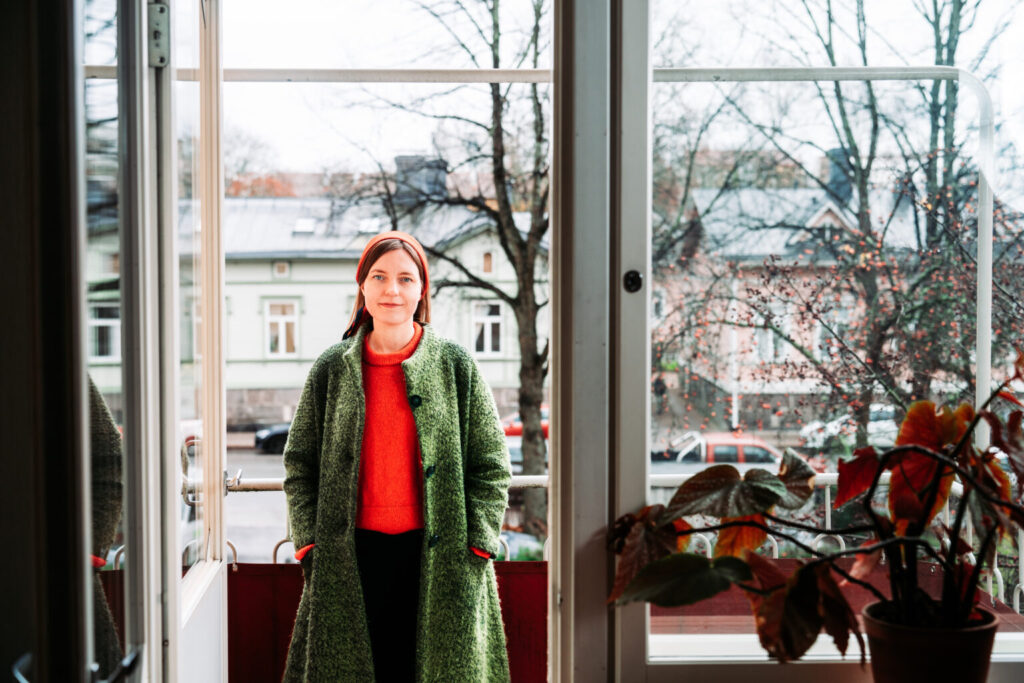 En kvinna i grannröd skjorta står vid stora fönster. 