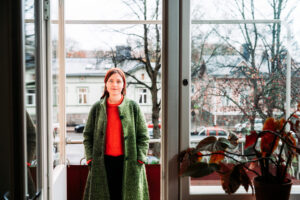 En kvinna i grannröd skjorta står vid stora fönster.