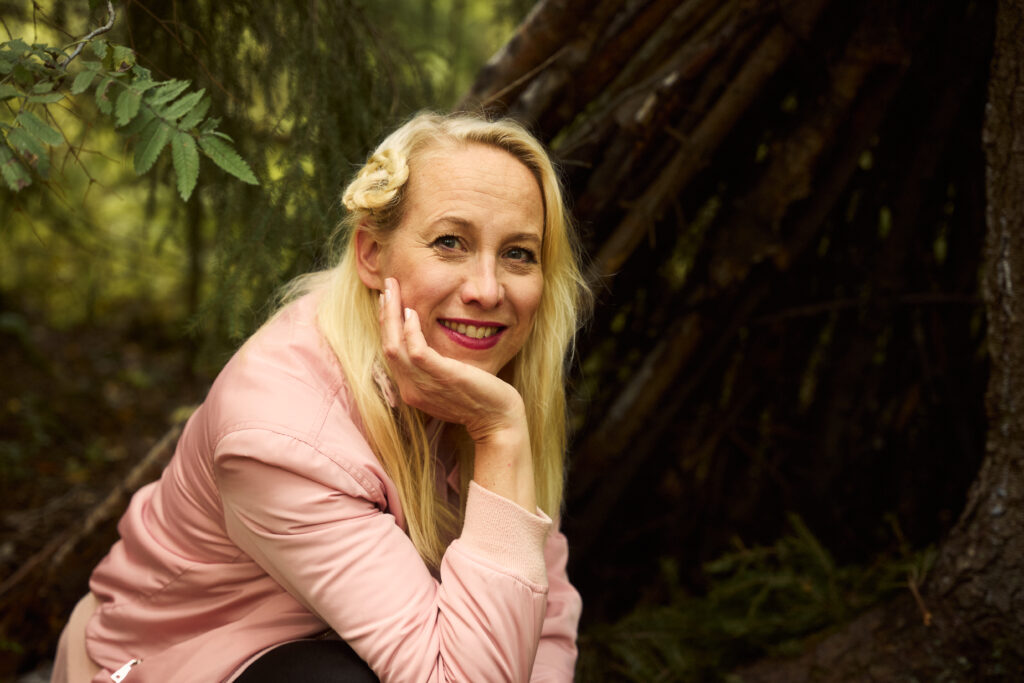 En blond kvinna sitter ute i naturen. 