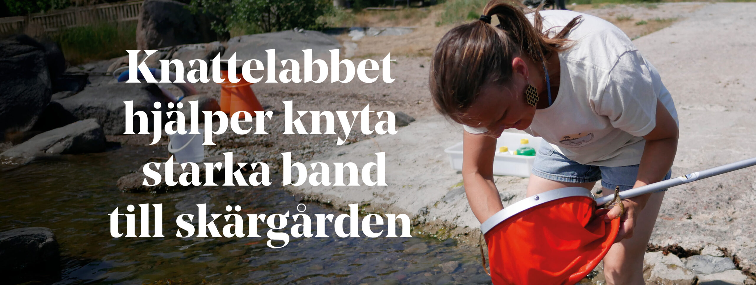 En kvinna står i vattenbrynet med en håv.