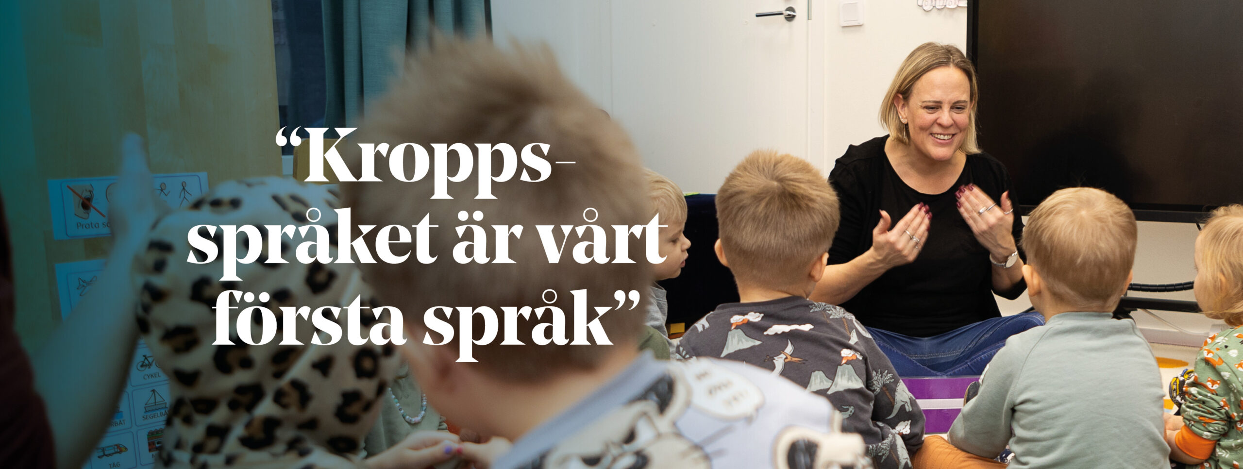 En kvinna sitter på golvet i ett daghem omringad av barn.