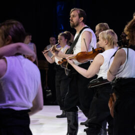 Bilden föreställer musikanter som spelar gitarr och fiol och sjunger.