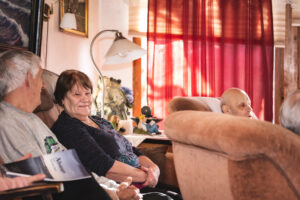 Bilden föreställer tre seniorer som sitter i en soffgrupp i ett vardagsrum.