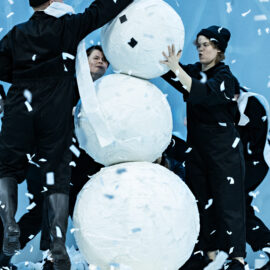 Några personer iklädda svarta halare gör en snögubbe.