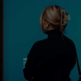 En kvinna står med ryggen mot kameran och tittar på målningar i guldram på ett museum.