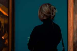 En kvinna står med ryggen mot kameran och tittar på målningar i guldram på ett museum.