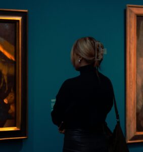En kvinna står med ryggen svängd mot kameran och tittar på verk i museet Ateneum.